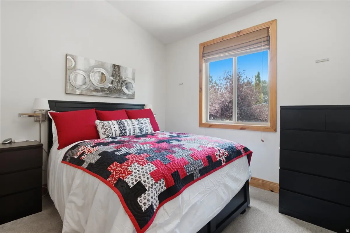 Bright room featuring a large window with natural wood trim, a vaulted ceiling, and carpet flooring