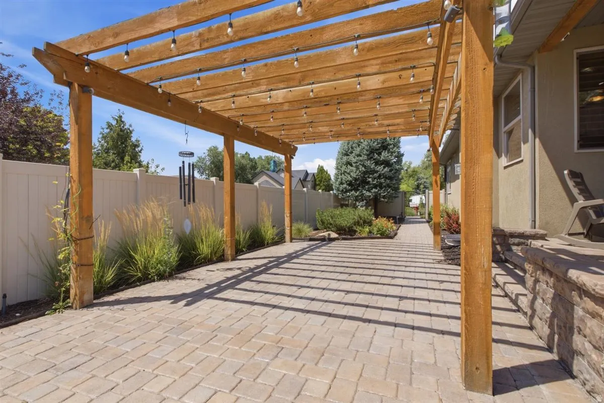 Paved patio area featuring a wooden pergola with string lighting