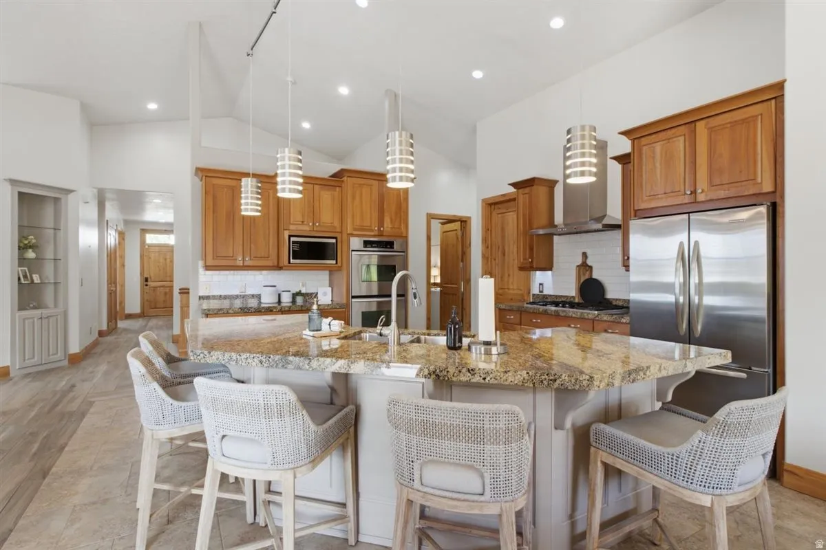 Spacious kitchen featuring a large central island with seating, granite countertops, wood cabinetry, and stainless steel appliances