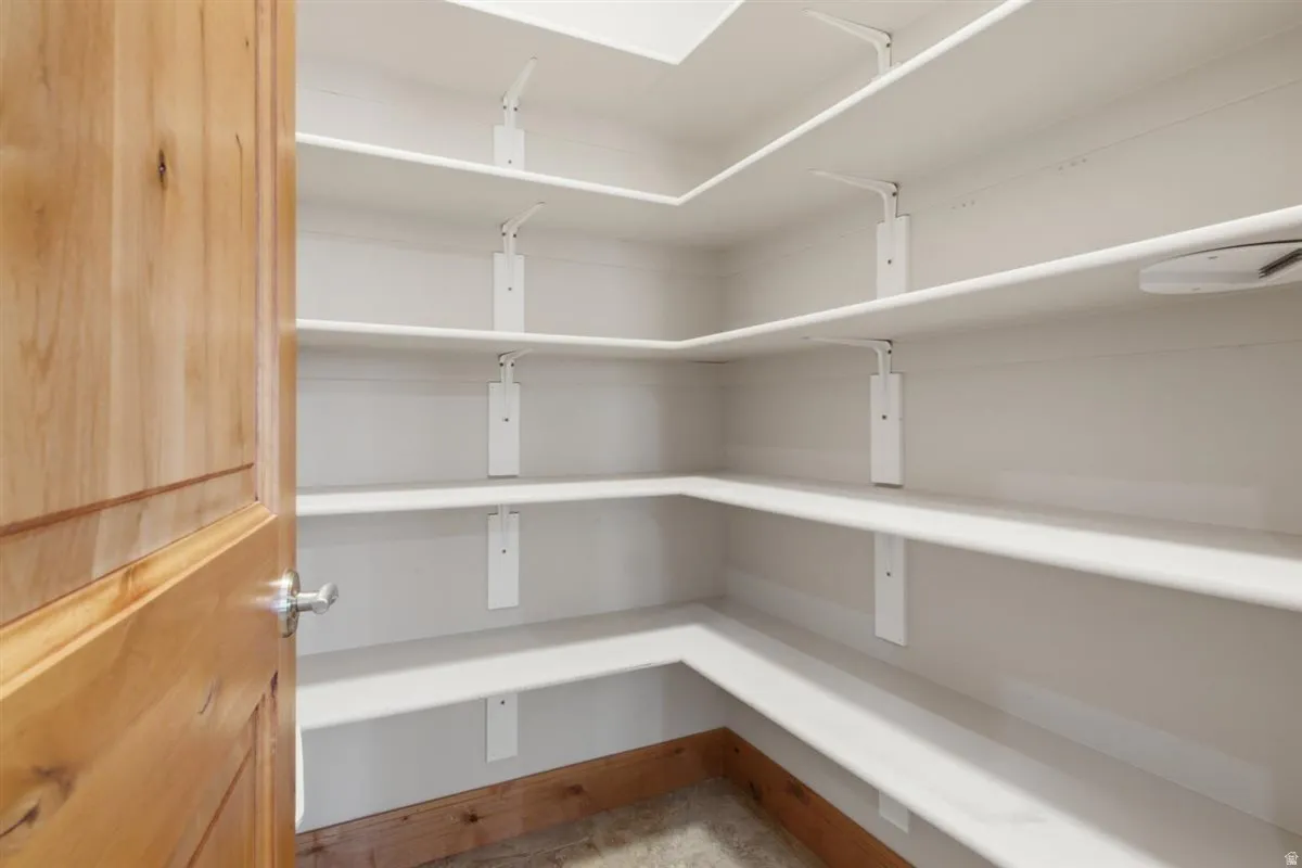 Spacious pantry featuring extensive white shelving, a natural wood-finish door, and integrated lighting