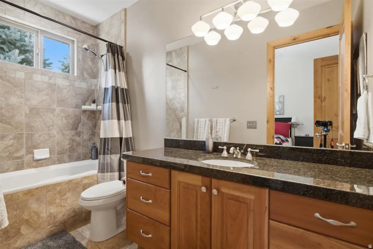 Bathroom featuring a light wood-finish vanity with a dark granite countertop, undermount sink, and chrome fixtures