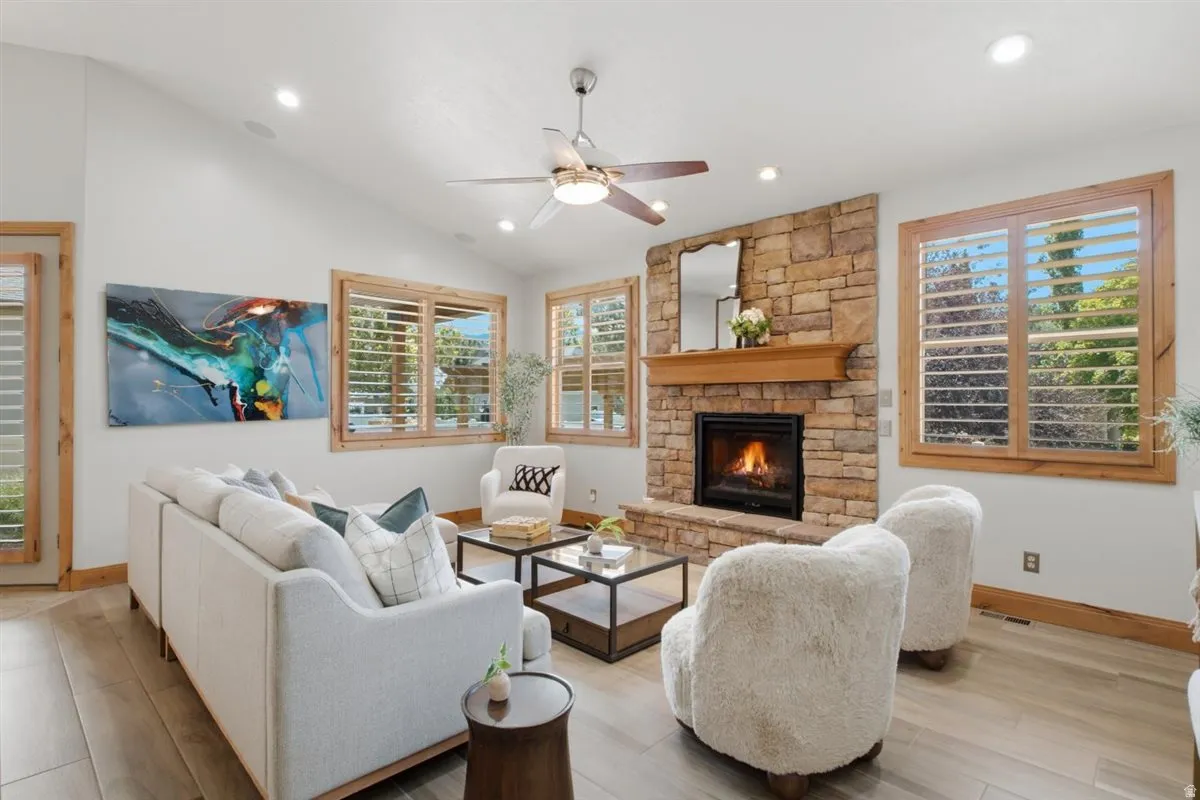 Living space featuring a stone-clad fireplace with a wood mantel, wood-finish flooring, and multiple windows with wood-framed plantation shutters