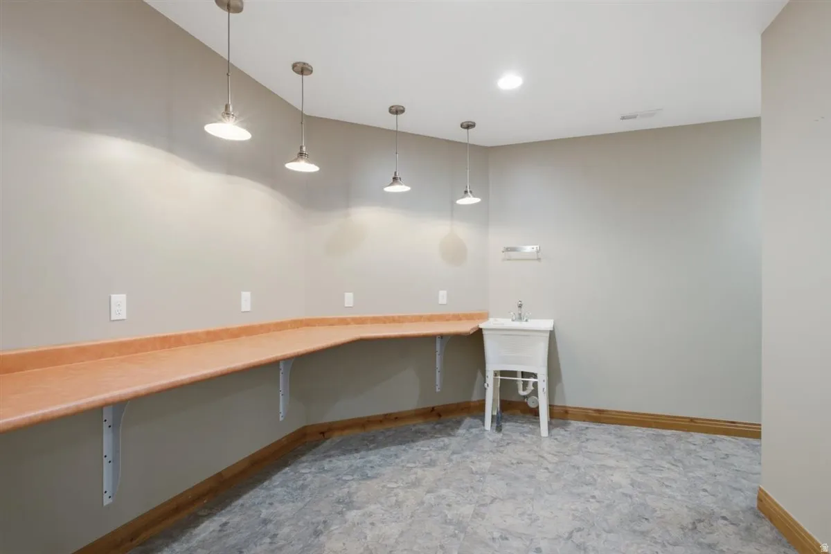 Utility room featuring expansive wraparound countertop, white utility sink, pendant lighting, recessed ceiling light, and durable flooring