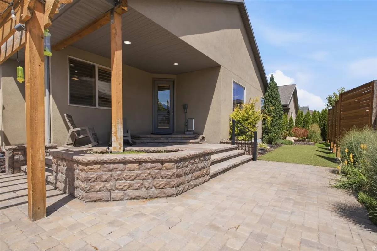 Expansive paver patio featuring a wood pergola and a stone-faced raised planter