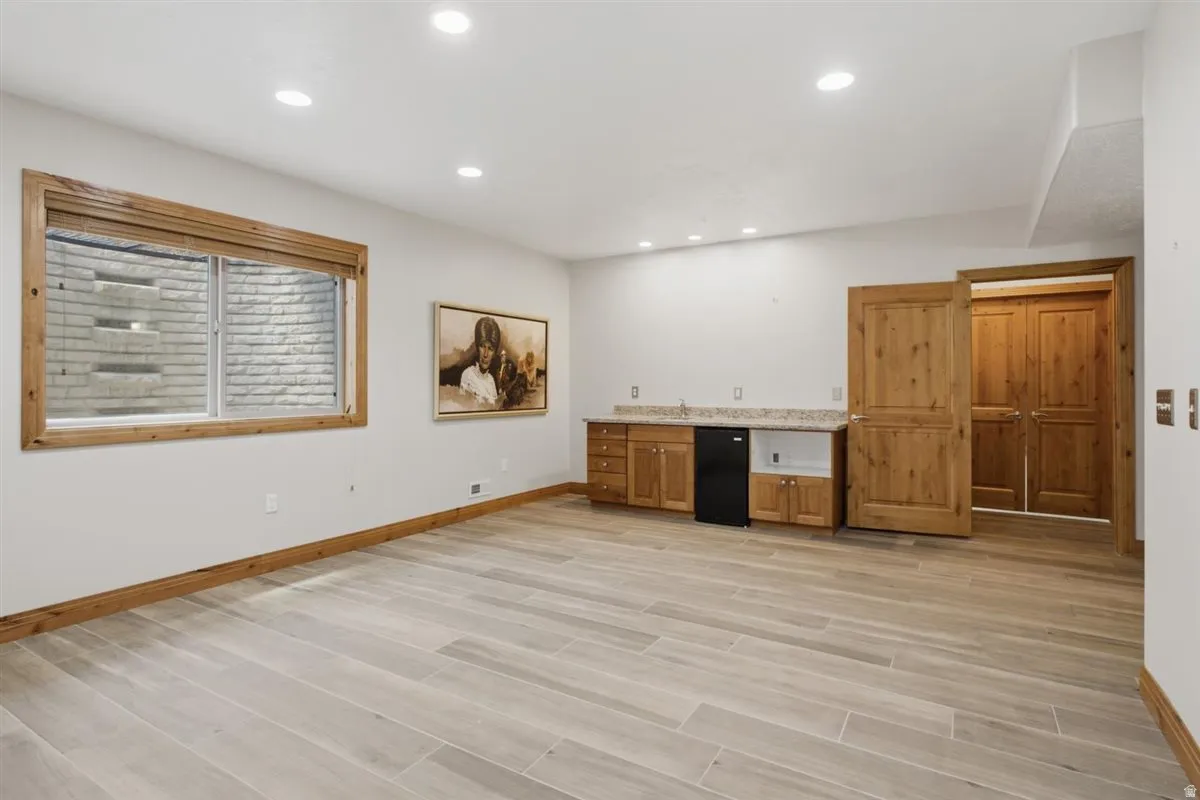 Spacious room featuring light wood-finish plank flooring, recessed lighting, and a built-in wet bar with wood cabinetry and a mini-refrigerator