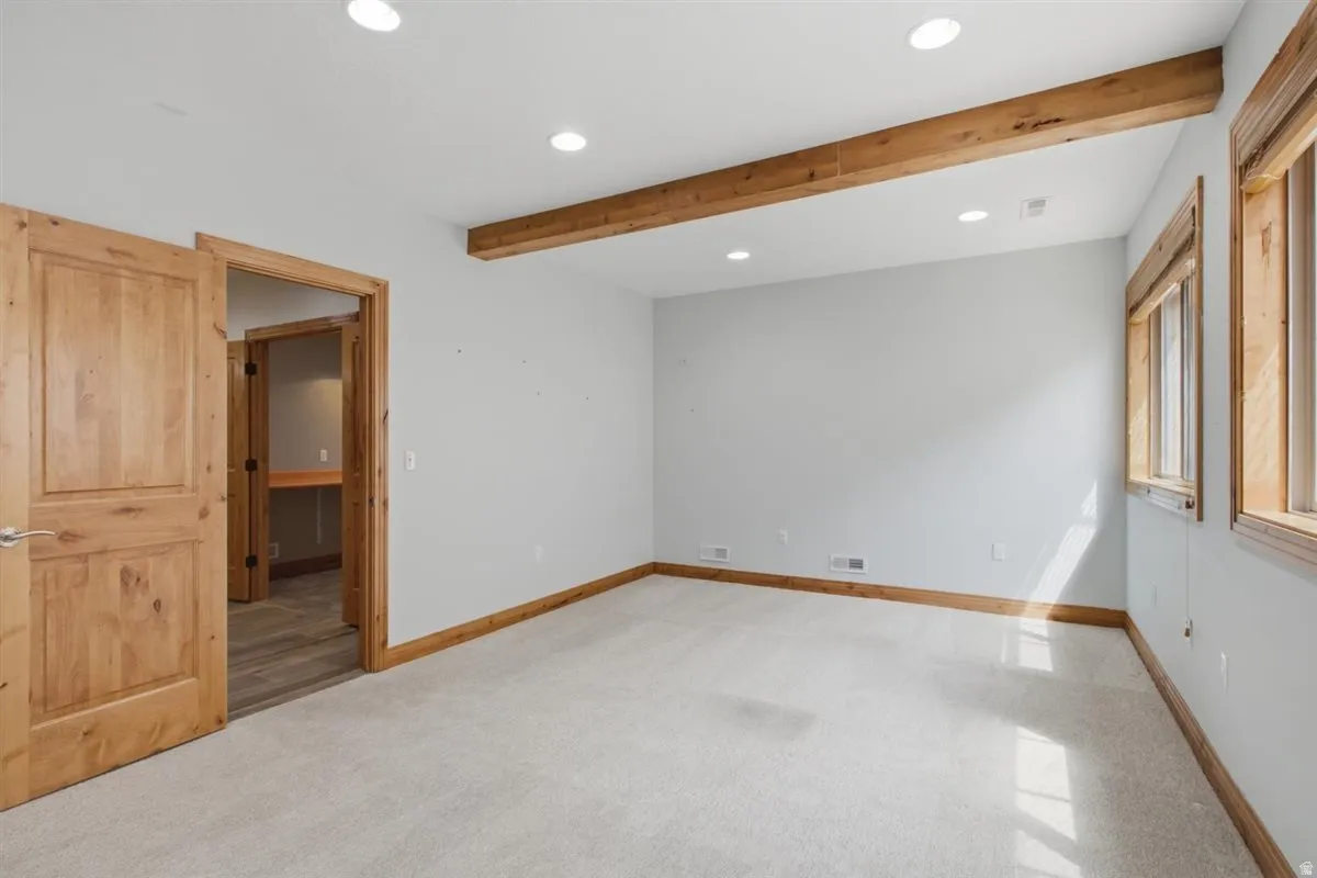 Spacious room featuring light-toned carpeting, recessed lighting, and exposed wood ceiling beams