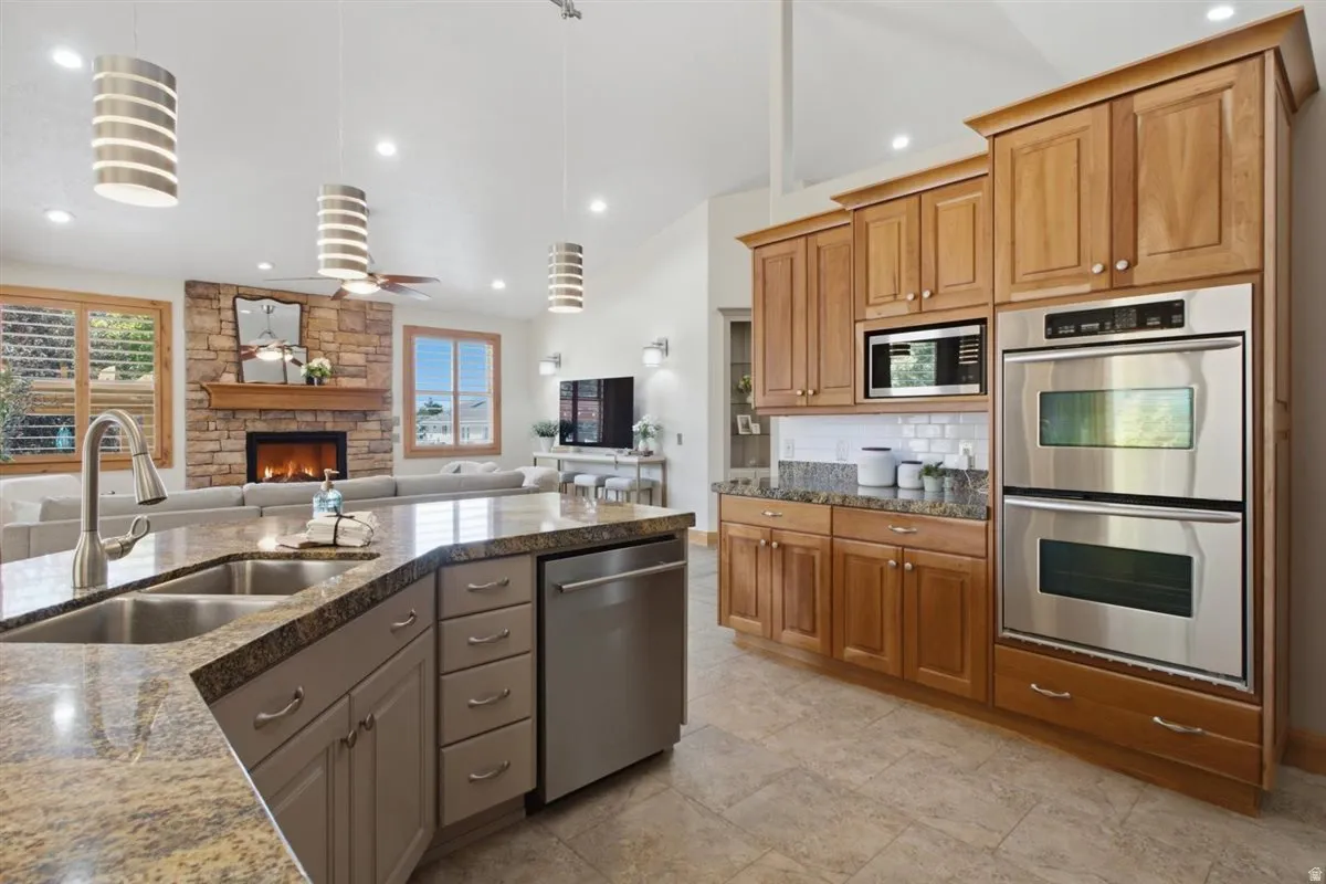 Open-concept kitchen featuring an island with a double basin sink, stainless steel appliances, and abundant wood cabinetry