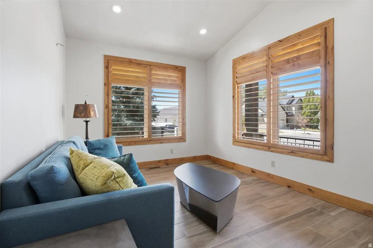 Room featuring wood-finish flooring, two large windows with plantation shutters, recessed ceiling lighting, and a vaulted ceiling