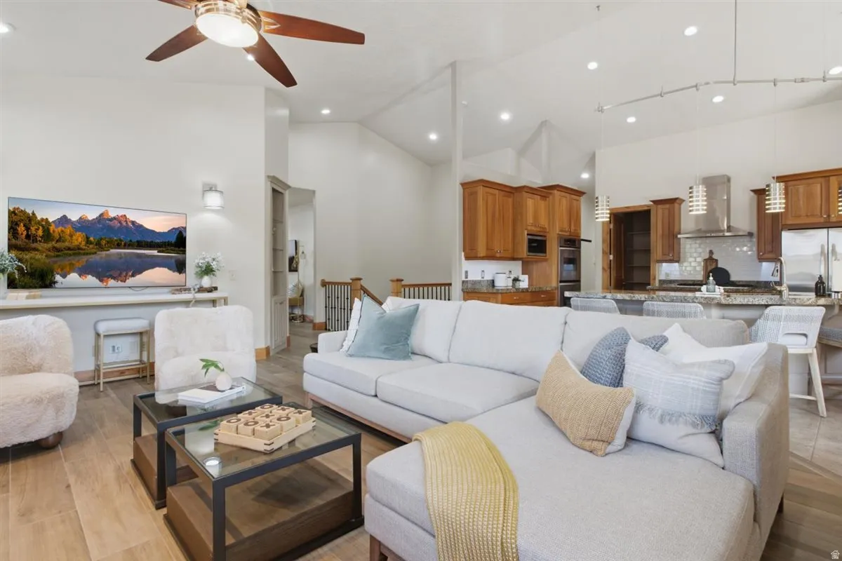 Open-concept living space featuring vaulted ceilings, wood-finish flooring, a kitchen with cabinetry, stainless steel appliances, and an island with bar seating