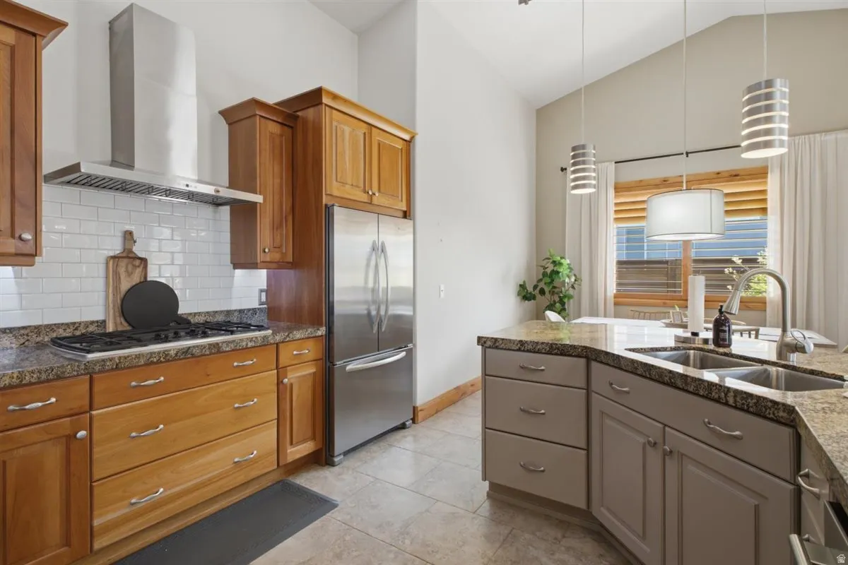 Kitchen featuring stainless steel appliances, granite countertops, white subway tile backsplash, and vaulted ceilings with pendant lighting