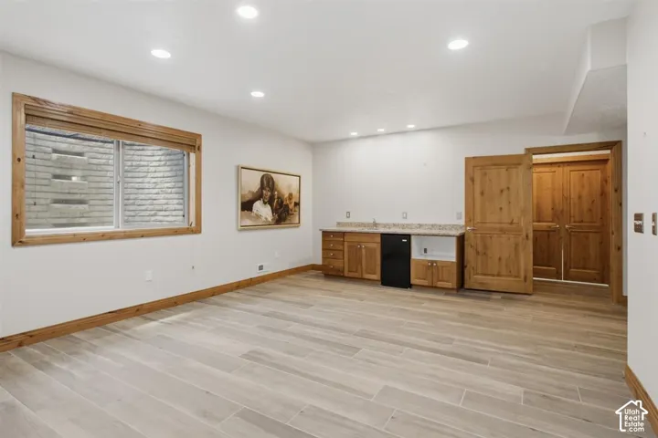 Spacious room featuring light wood-finish plank flooring, recessed lighting, and a built-in wet bar with wood cabinetry and a mini-refrigerator