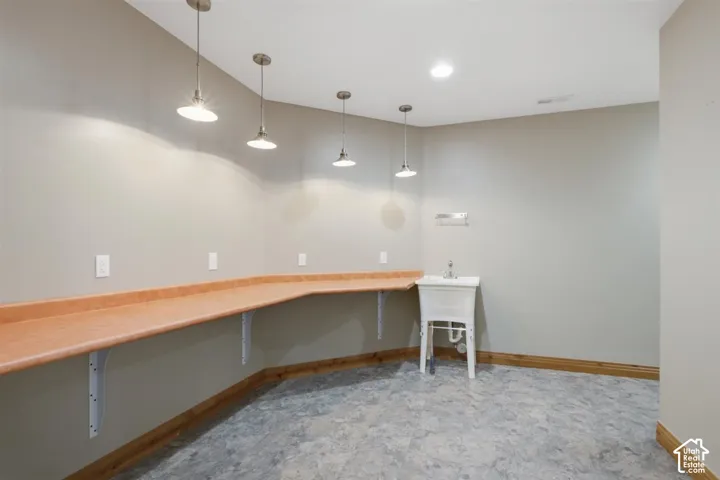 Utility room featuring expansive wraparound countertop, white utility sink, pendant lighting, recessed ceiling light, and durable flooring