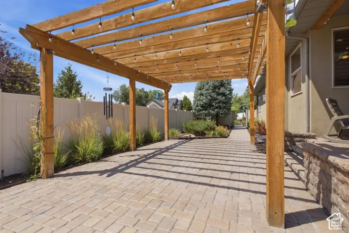 Paved patio area featuring a wooden pergola with string lighting