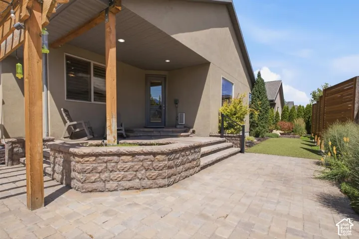 Expansive paver patio featuring a wood pergola and a stone-faced raised planter