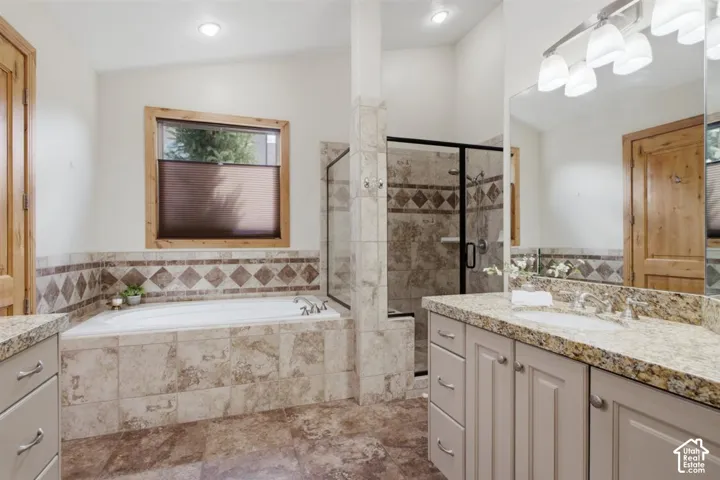 Bathroom featuring a built-in tub with tile surround, a separate glass-enclosed shower, a double vanity with stone countertops, and wood-paneled doors