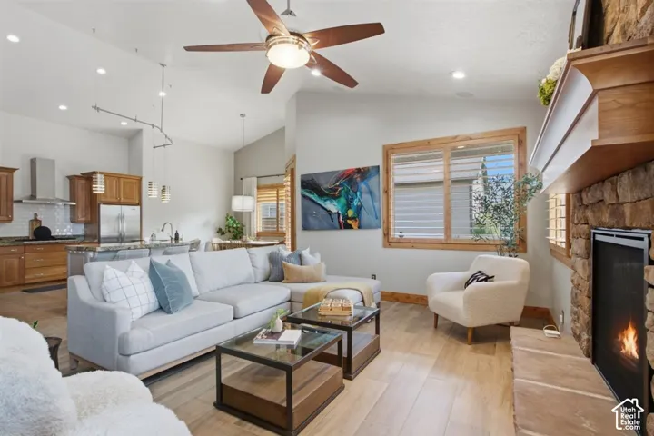Vaulted ceiling living area with a stone fireplace, wood-finish flooring, and a ceiling fan