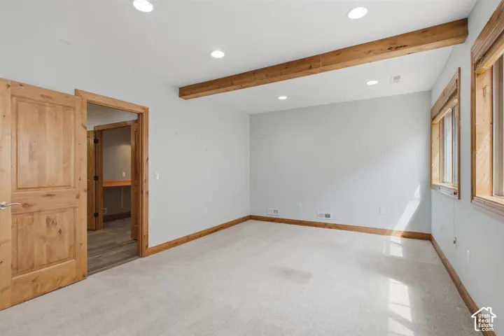 Spacious downstairs room featuring light colored carpeting, recessed lighting, and exposed wood ceiling beams