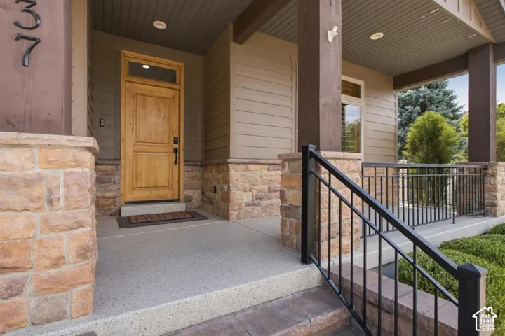 Welcoming front entry featuring a natural wood door with transom window, stone veneer accents, durable concrete porch, wrought iron railing, and recessed lighting