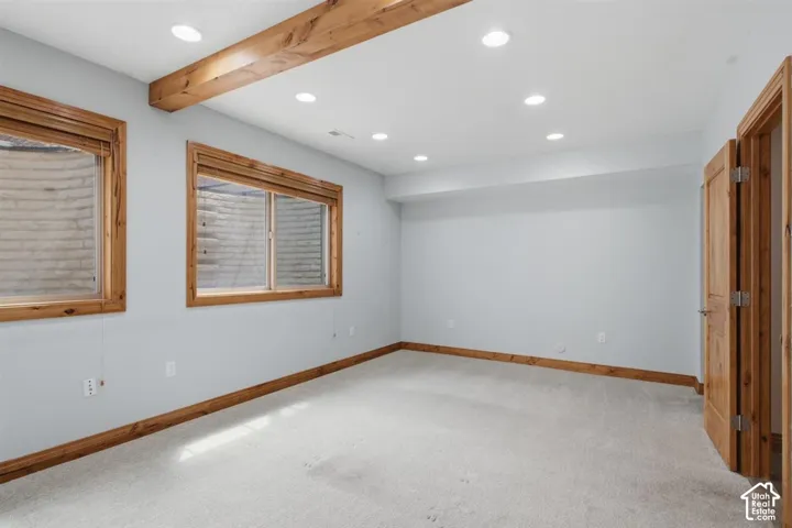 Carpeted  downstairs room featuring two egress windows with wood trim, a wood-finish ceiling beam, recessed lighting, and wood-paneled doors