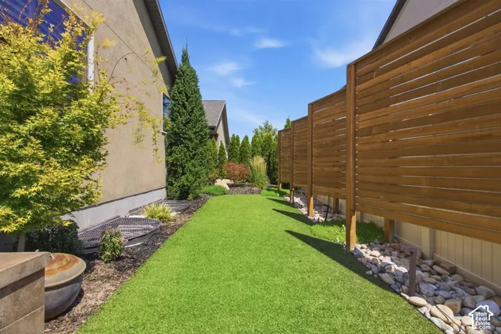 Landscaped side yard featuring artificial turf, a horizontal wood privacy  fence, mature trees, and a rock bed