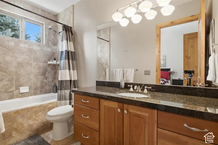 On suite bathroom featuring a light wood-finish vanity with a dark granite countertop, undermount sink, and chrome fixtures