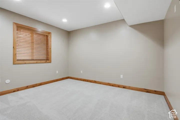 Basement carpeted room featuring a window with wood blinds and wood trim, recessed lighting, and neutral wall paint