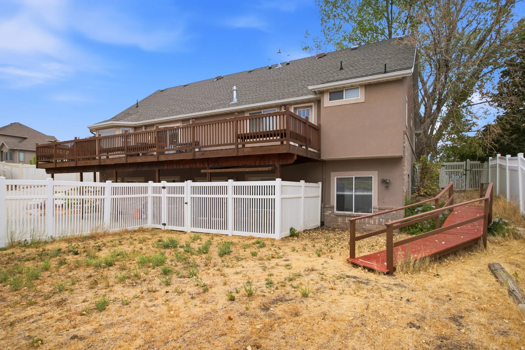 Spacious rear exterior featuring a full-width upper deck with wood railings, a lower-level access ramp, and white privacy fencing