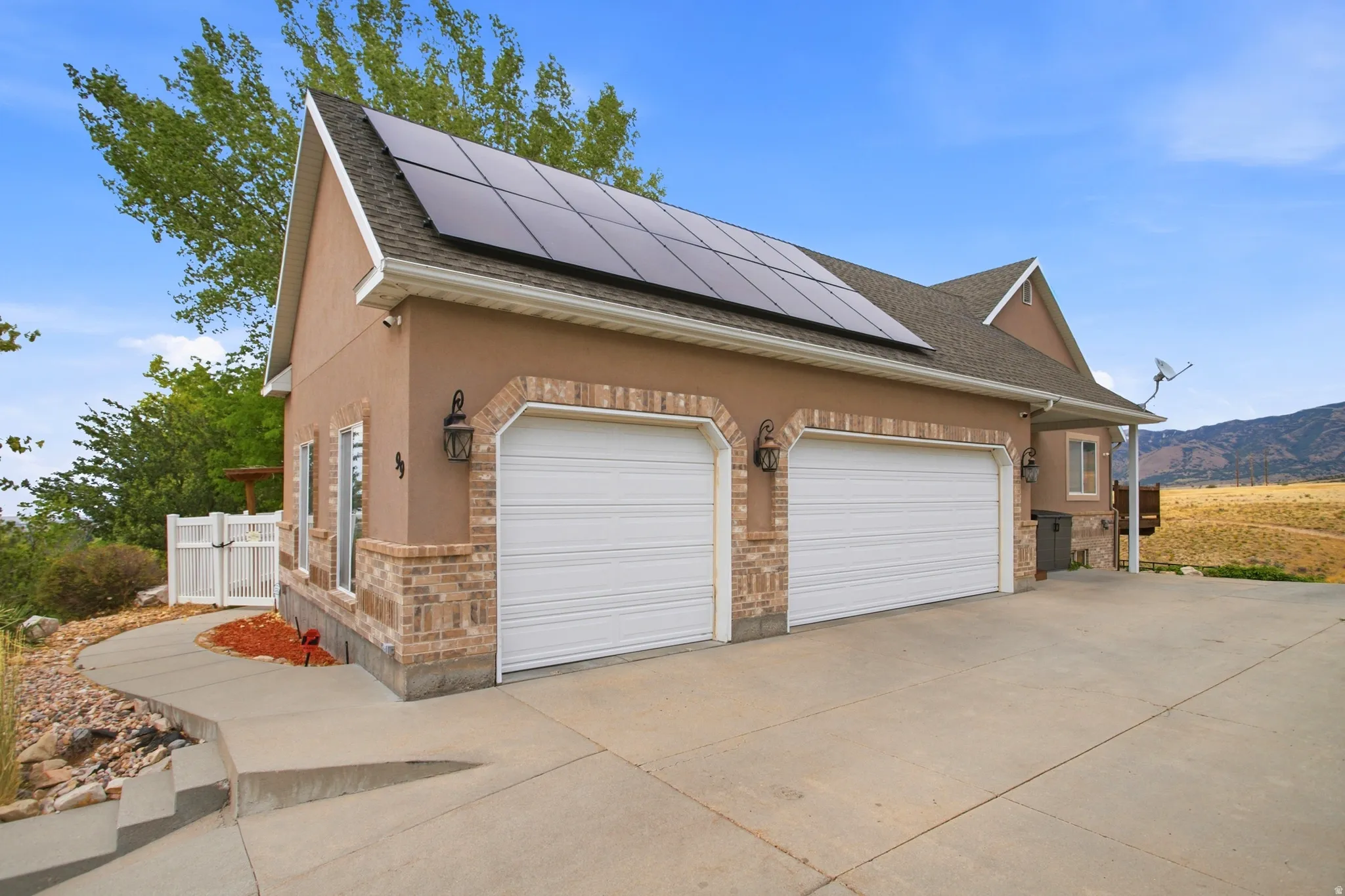 Exterior featuring a two-car garage with brick archways, stucco siding, and solar panels on the roof