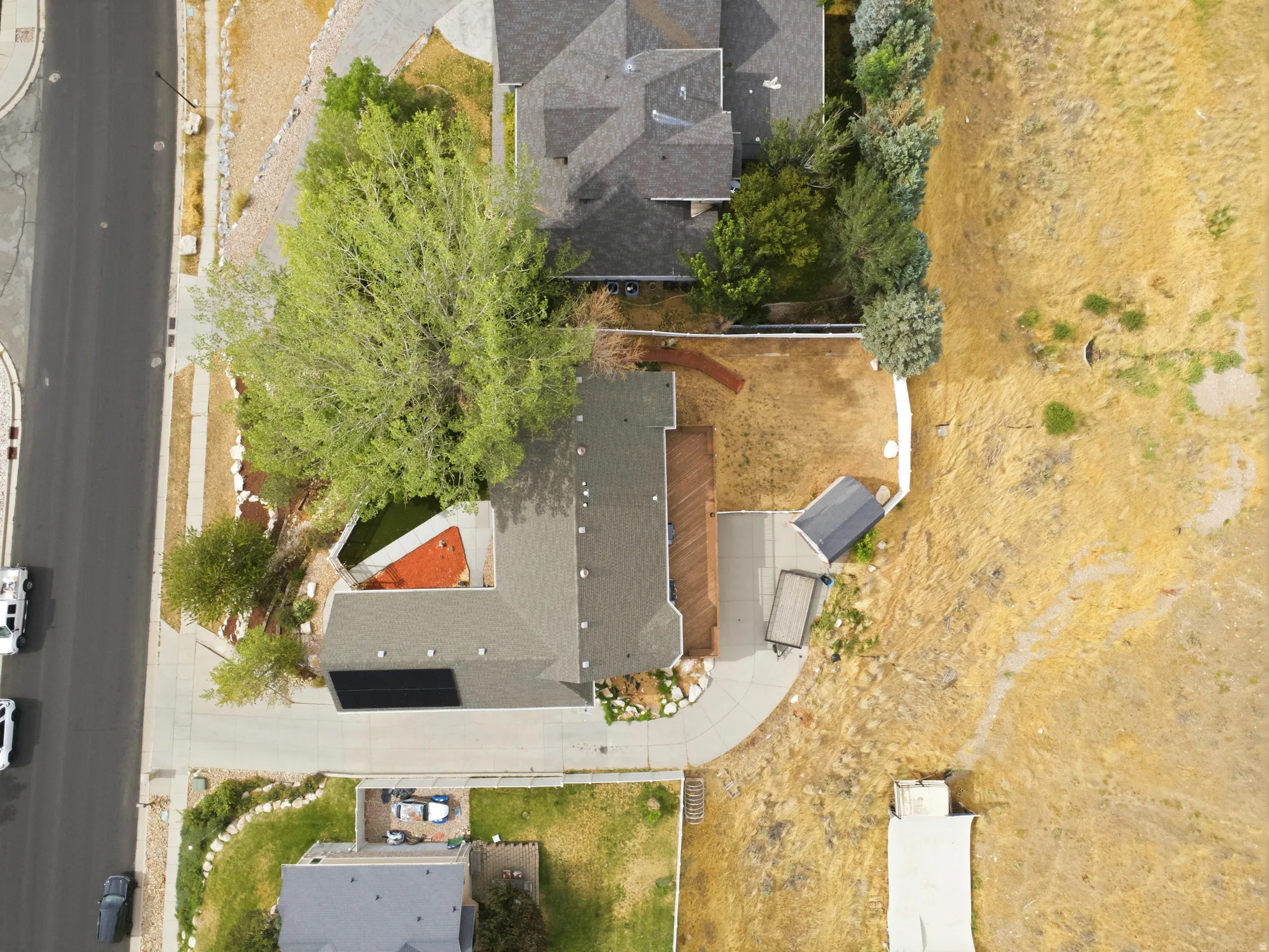 Property featuring a dark shingle roof, a generously sized backyard, a paved driveway, and established trees