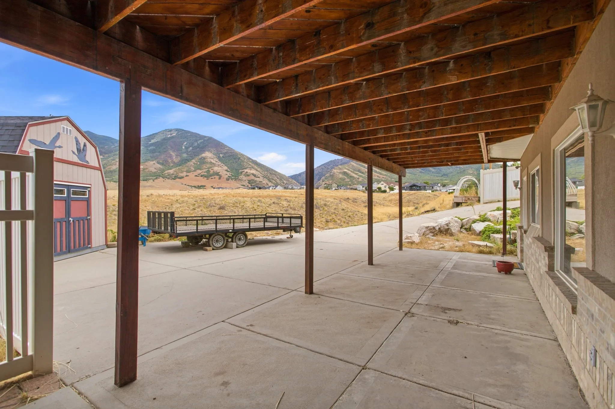 Expansive concrete patio with a wooden beam ceiling, supported by sturdy posts