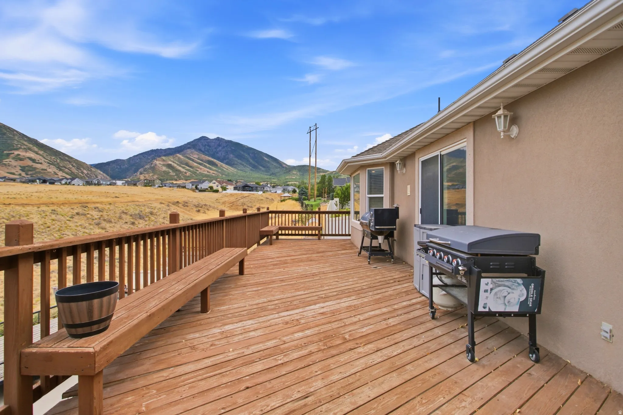 Expansive outdoor deck featuring wood flooring and railings, a built-in wood bench, and direct access to the interior via a sliding glass door
