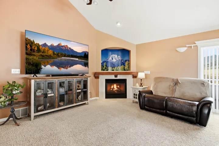 Vaulted ceiling featuring recessed lighting, a built-in fireplace with a stone hearth and wood mantel, and sliding glass doors with vertical blinds