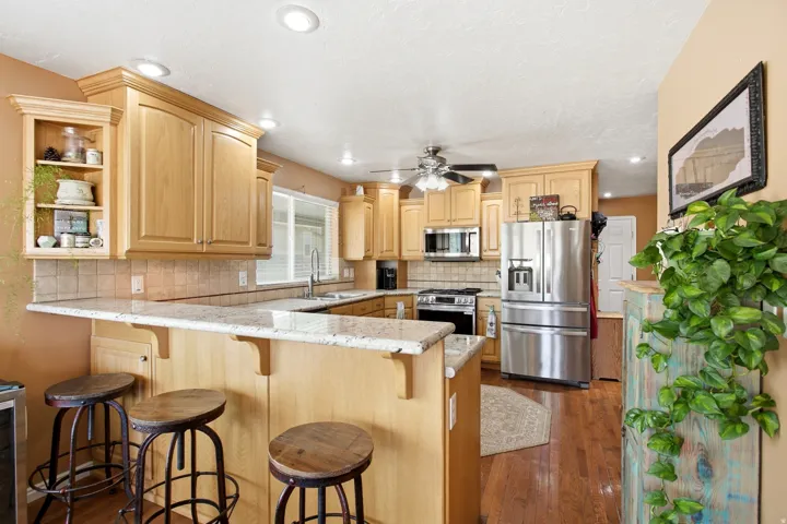 Kitchen featuring light wood cabinetry, recessed lighting, stainless steel appliances, a tiled backsplash, and a breakfast bar with a stone-finish countertop