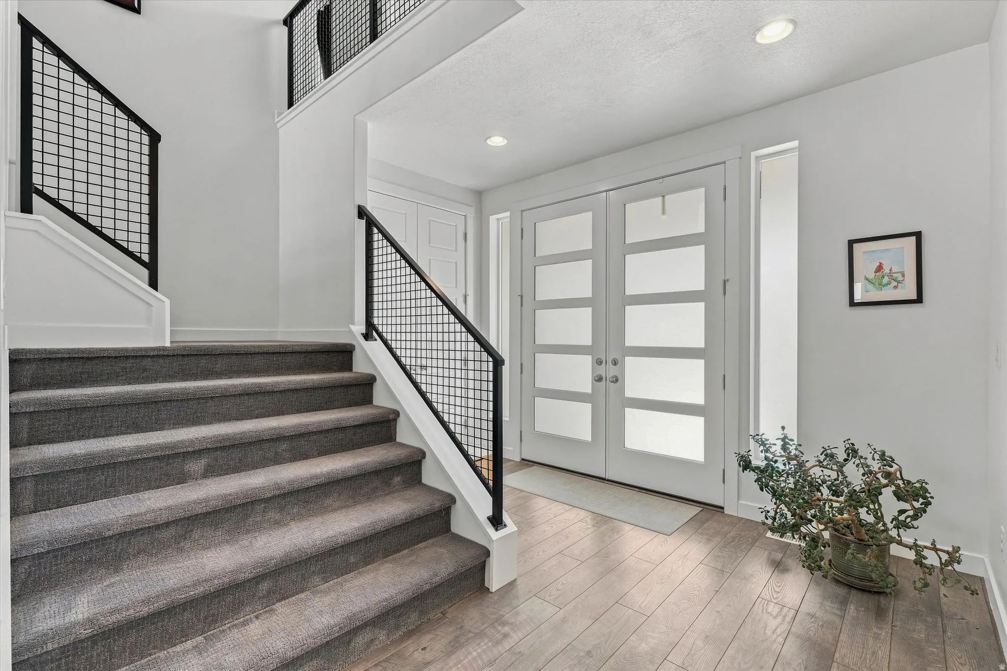 Entry foyer featuring light wood-finish flooring, a contemporary double door entry with frosted glass panels, and a staircase with gray carpeting and modern metal railings