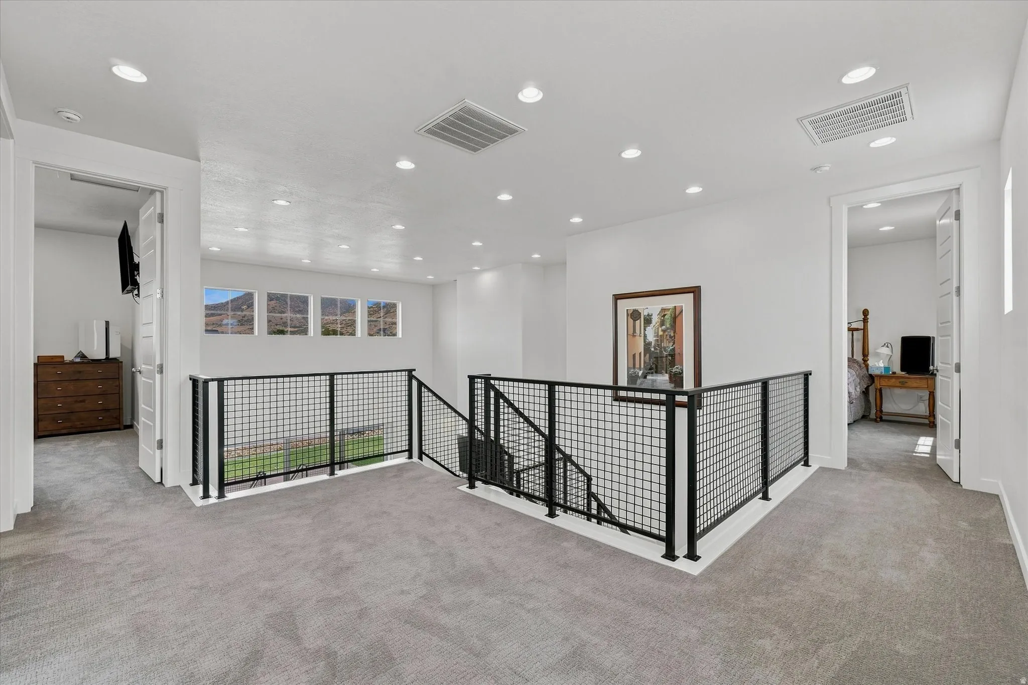 Upper-level landing featuring light gray carpeting, recessed lighting, and a contemporary black metal grid railing system