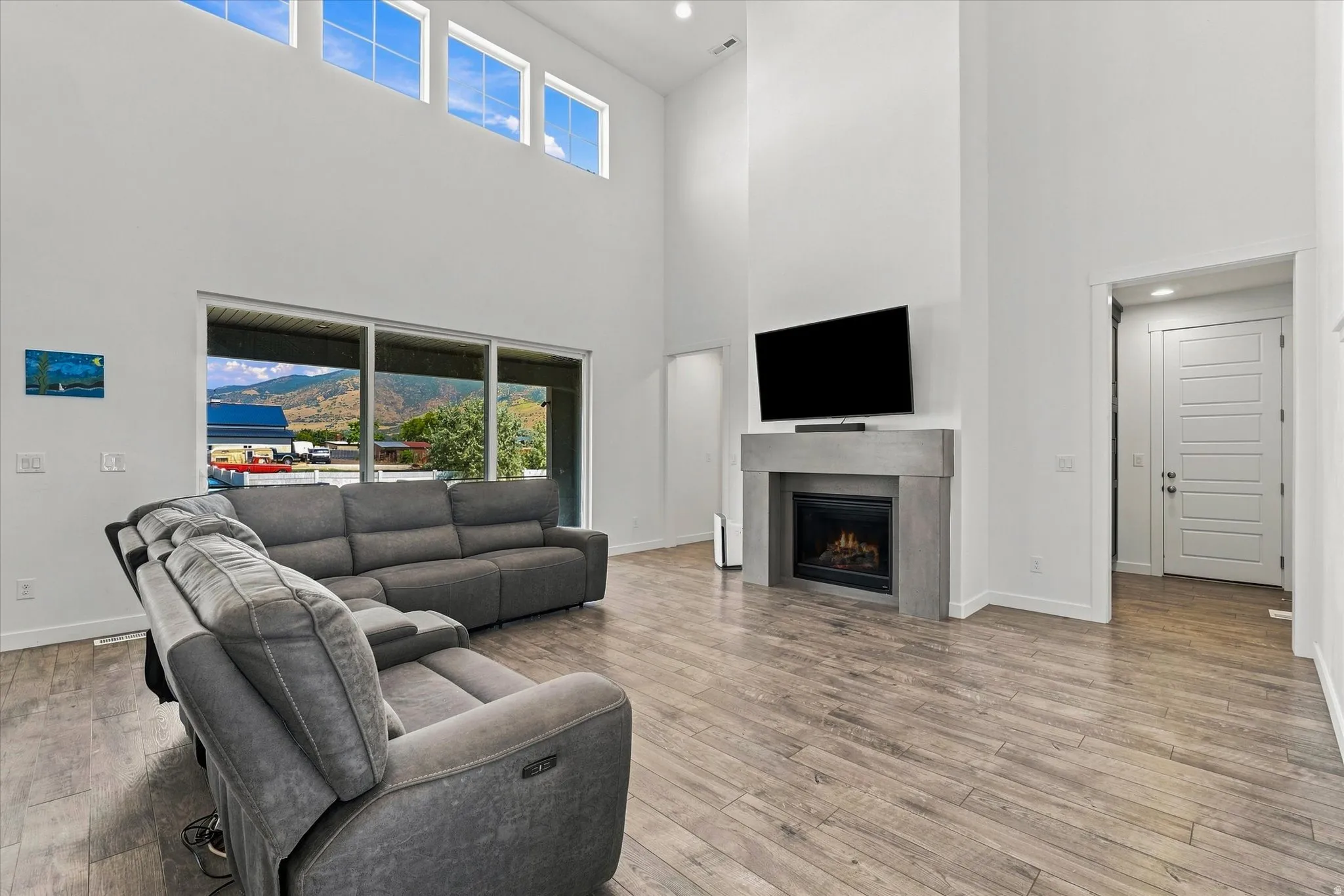 Spacious living area featuring high ceilings, wood-finish flooring, a contemporary fireplace with a stone surround, and large windows providing abundant natural light