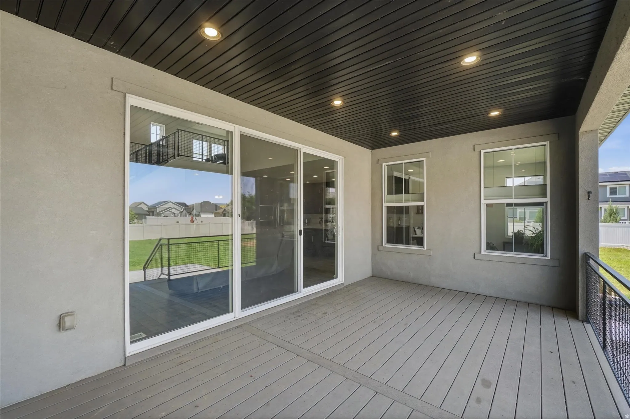 Covered patio featuring a slatted ceiling with recessed lighting, gray composite decking, stucco exterior, and sliding glass doors