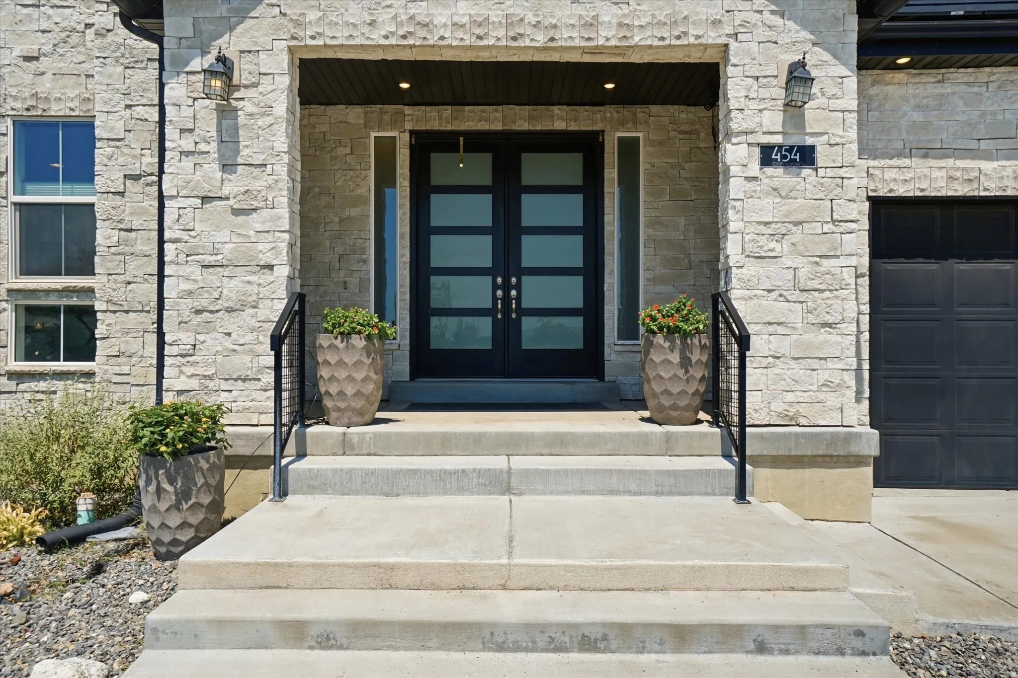 Stone veneer exterior featuring a modern double-door entry with frosted glass panels, concrete steps, and black metal railings