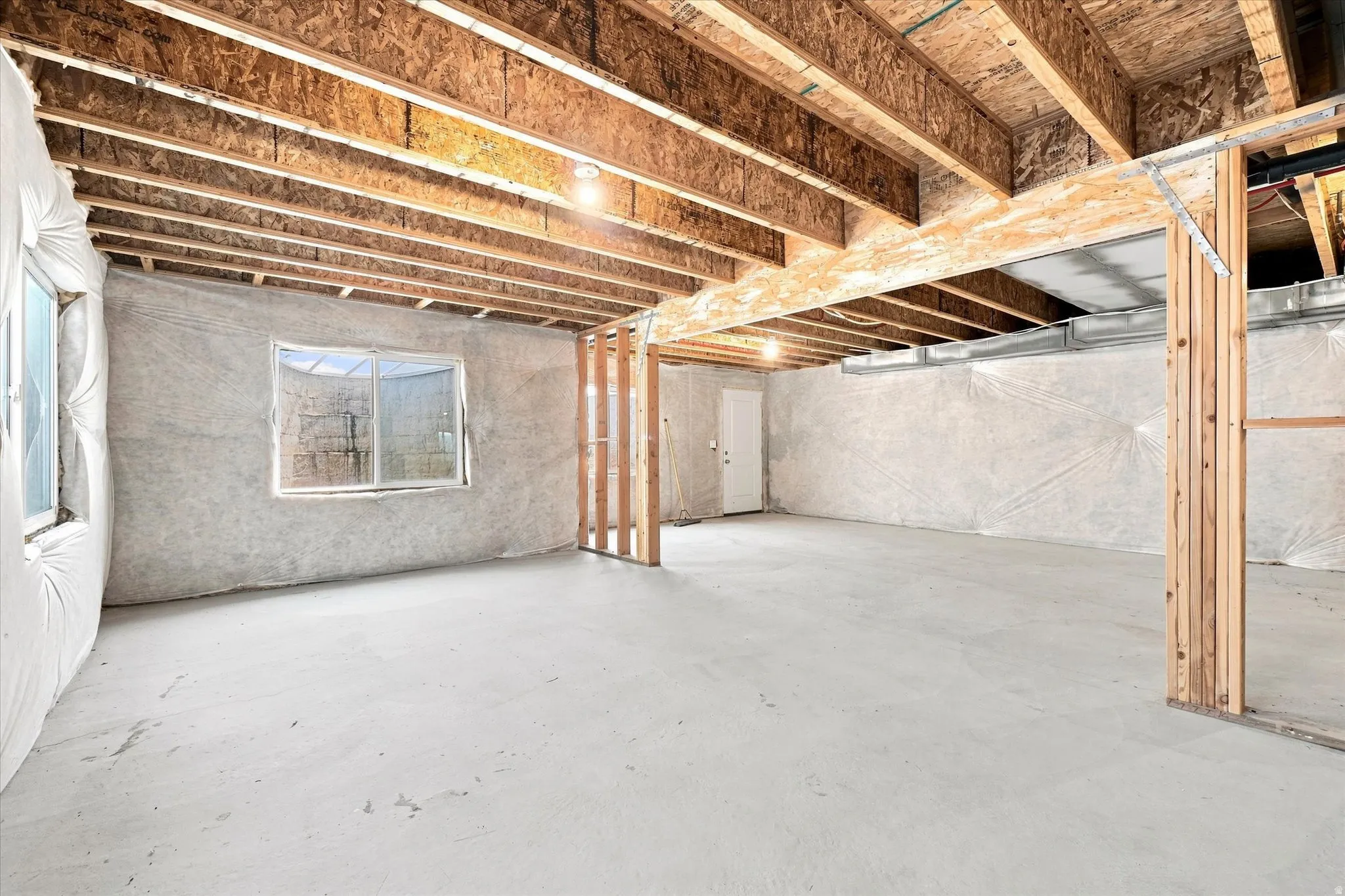 Unfinished basement featuring exposed wood joists, concrete flooring, and multiple windows