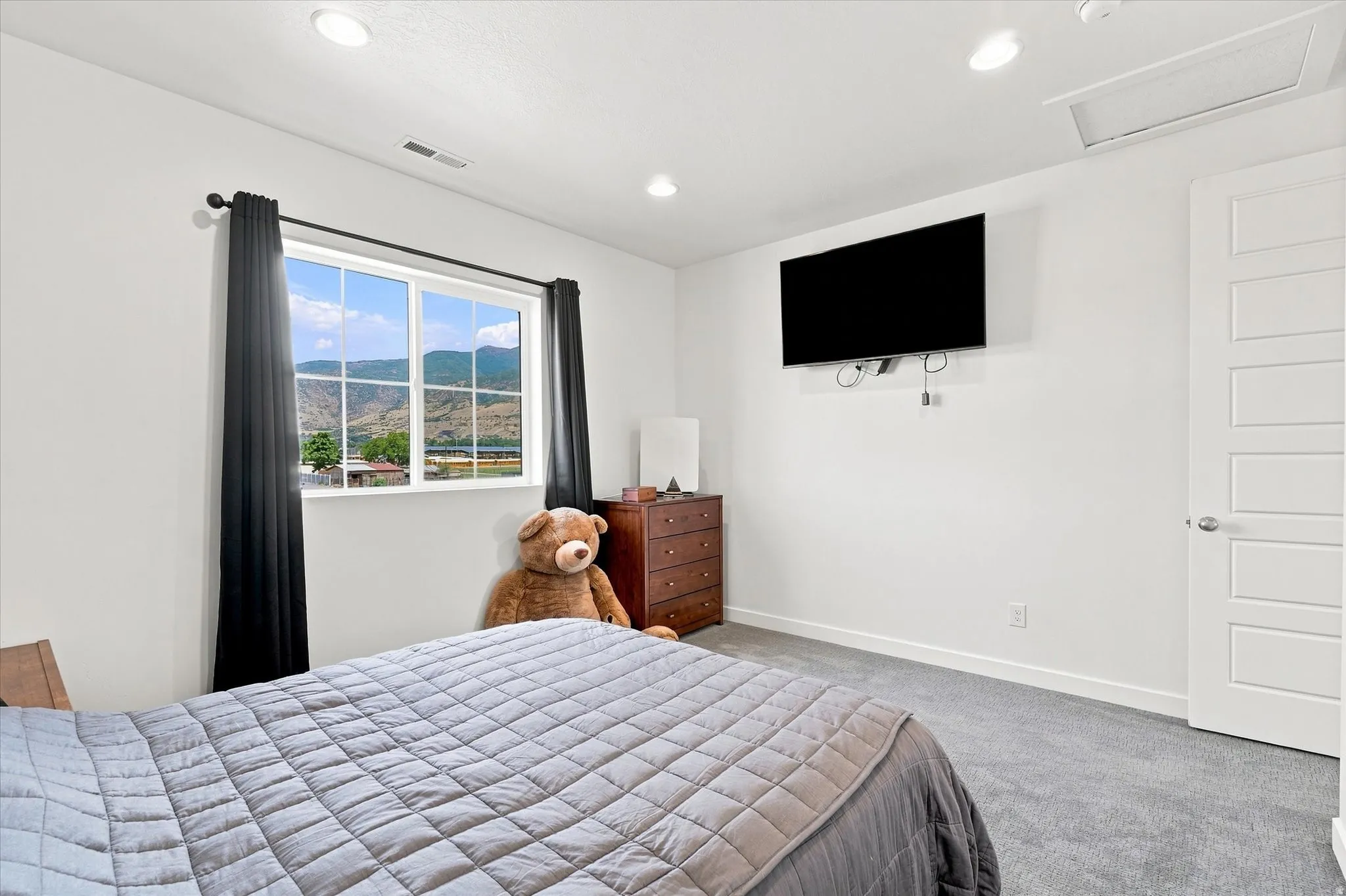 Window with mountain scenery, recessed ceiling lighting, wall-mounted television, multi-panel interior door, and grey carpeting