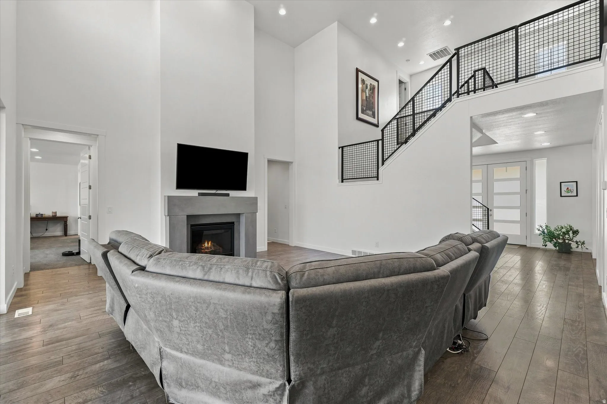 Spacious living area featuring high ceilings, a contemporary fireplace with a stone-finish mantle, and wood-finish flooring