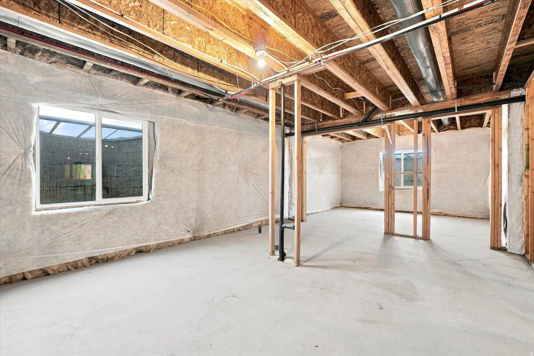 Unfinished lower level featuring exposed wood beam ceiling, concrete flooring, and multiple windows