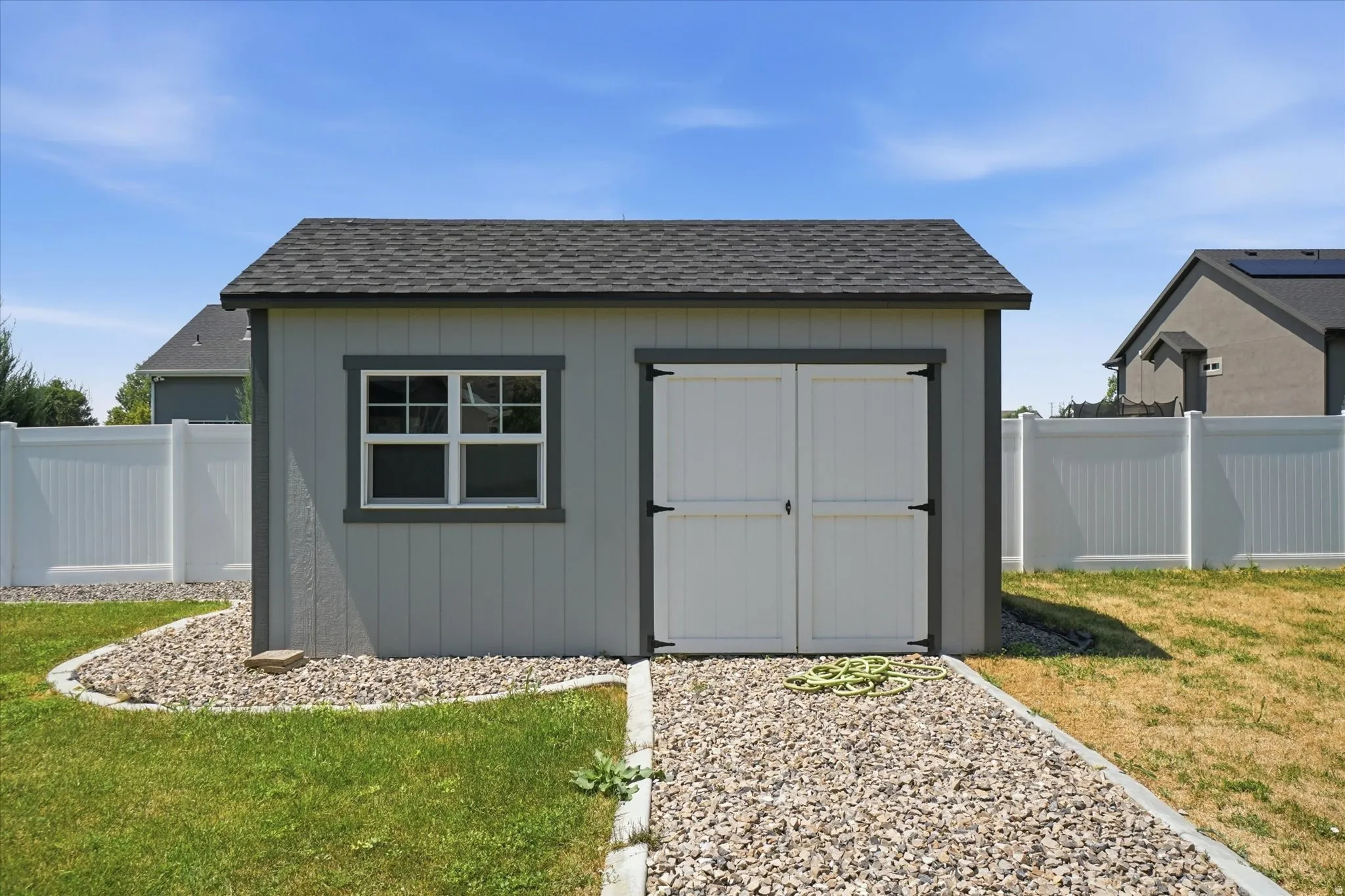Detached storage shed featuring vertical siding, a gabled roof with asphalt shingles, and white double doors