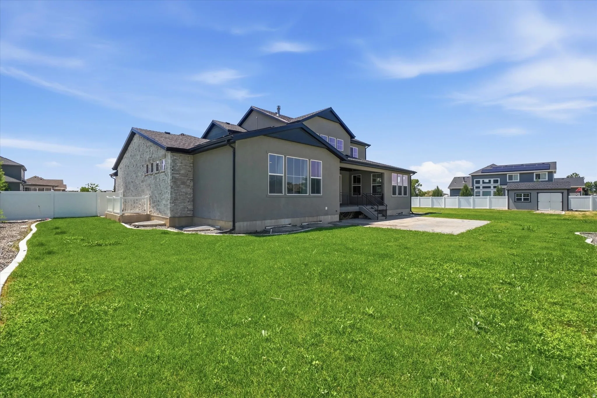 Expansive green lawn with a concrete patio, privacy fencing, and a detached two-car garage