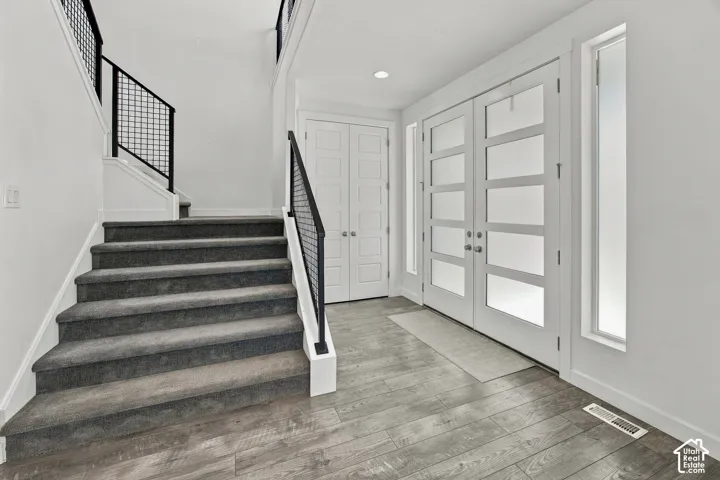 Entryway featuring wood-finish flooring, a contemporary staircase with metal grid railing, and double entry doors with frosted glass panels