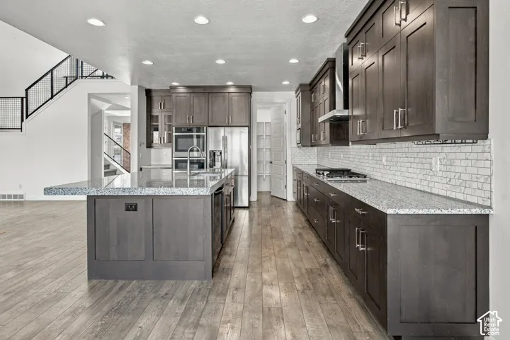 Kitchen featuring engineered wood flooring, dark wood cabinetry, light-toned countertops, subway tile backsplash, and stainless steel appliances
