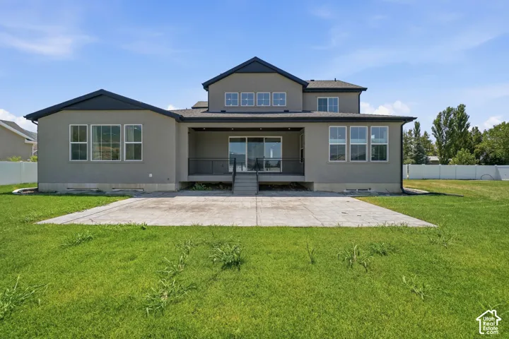 Expansive backyard with a concrete patio, covered patio, multiple windows, and a sliding glass door