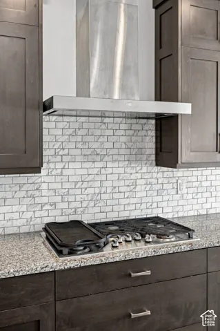 Stainless steel range hood over gas cook top with a mosaic tile backsplash