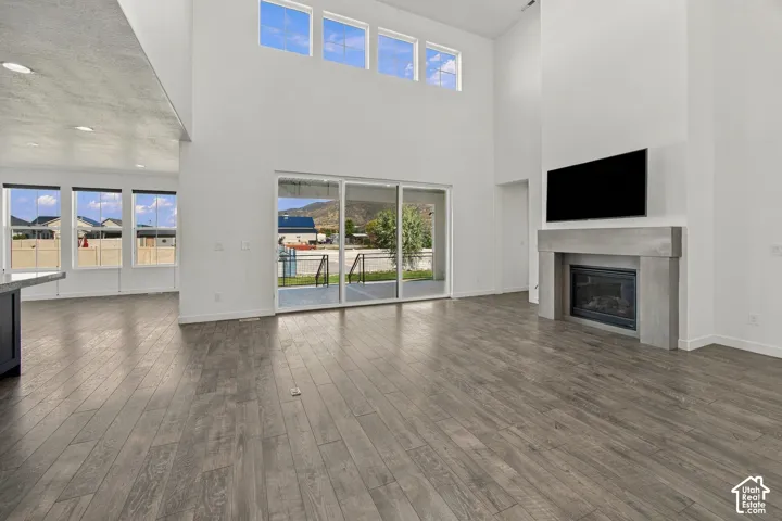 Spacious living area featuring high ceilings, engineered wood flooring, a contemporary fireplace with a stone-finish mantle, large sliding glass doors, and upper transom windows