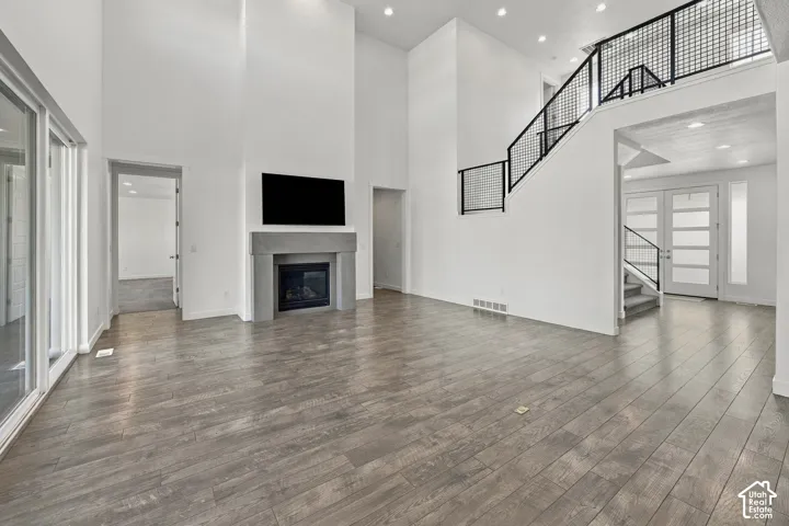 Expansive open-concept living area featuring wood-finish flooring, a contemporary fireplace with a stone-finish mantel, and a multi-level ceiling